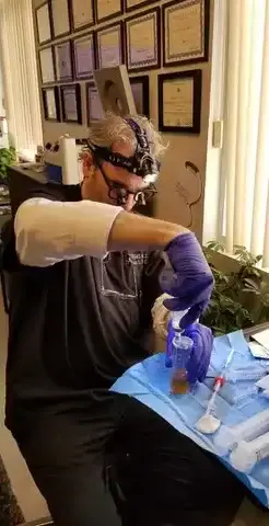 Thomas Pulice PA-C preparing PRP for P-Shot treatment at Las Vegas Aesthetics — surgical loupes, sterile technique, and credentials wall visible, Las Vegas NV